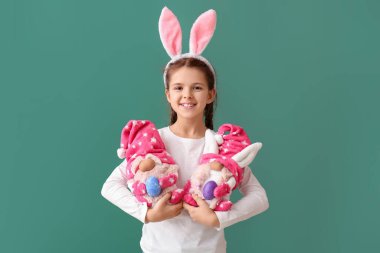 Tavşan kulaklı ve yeşil arka planda oyuncakları olan komik küçük bir kız. Paskalya kutlaması