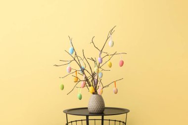 Vazo, ağaç dalları ve Paskalya yumurtaları renkli duvarların önünde.