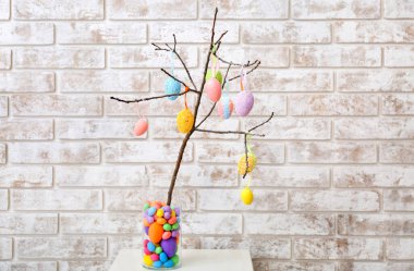 Ağaç dallı vazo ve hafif tuğla duvarın yanındaki masada farklı Paskalya yumurtaları.