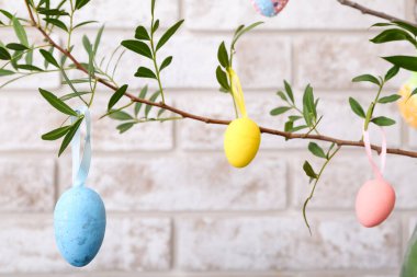 Paskalya yumurtaları olan yeşil ağaç dalları, hafif tuğla duvarın yanında, yakın plan.