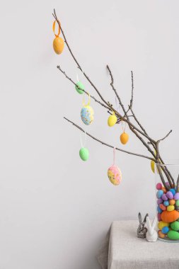 Farklı Paskalya yumurtaları olan ağaç dalları ve ışık duvarının yanındaki masada küçük oyuncak tavşanlar.