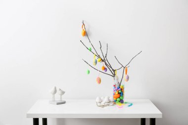 Farklı Paskalya yumurtaları olan ağaç dalları ve ışık duvarının yanındaki masada şık bir dekor.