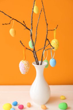 Ağaç dallı vazo ve beyaz ahşap masa üzerinde farklı Paskalya yumurtaları.