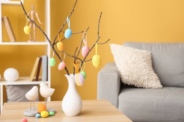 Ağaç dallı vazo ve oturma odasındaki ahşap masada farklı Paskalya yumurtaları.
