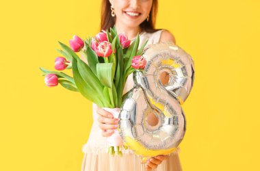 Sarı arka planda balon ve buketi olan genç kadın, yakın plan. Uluslararası Kadınlar Günü