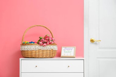 Paskalya yumurtaları ve çiçeklerle dolu Hasır sepet. Odadaki çekmecelerin üzerinde.