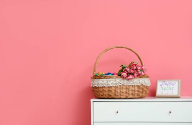 Paskalya yumurtaları ve çiçeklerle dolu Hasır sepet. Odadaki çekmecelerin üzerinde.