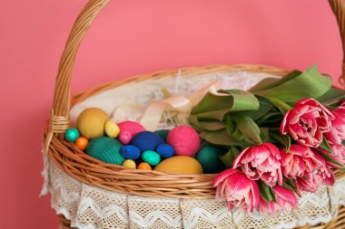 Paskalya yumurtaları ve pembe arka planda çiçekler olan hasır sepet, yakın plan.