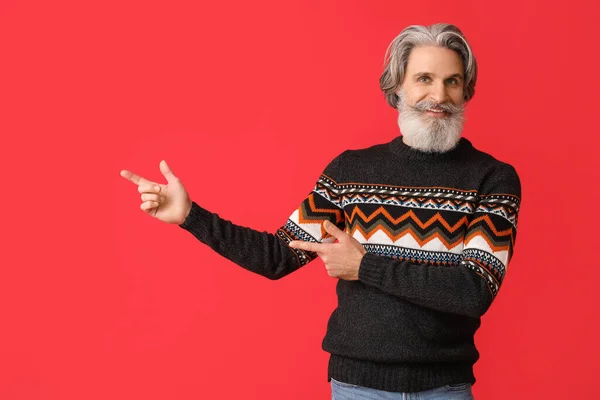 ハンサムなシニア男で編んだセーターPointingで何か上の赤の背景 — ストック写真
