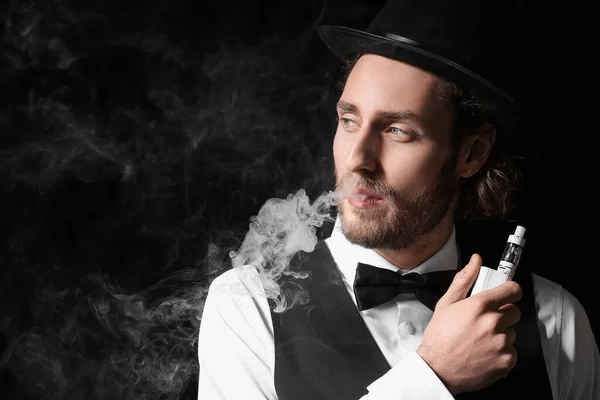 Vaping young man on black background