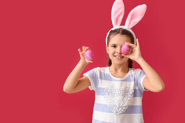 有兔子耳朵和红色背景的复活节彩蛋的小女孩很有趣 — 图库照片