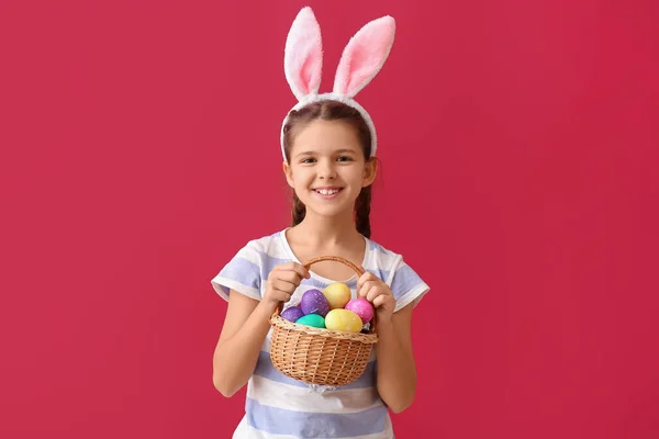 有趣的小女孩 有兔子耳朵和彩色背景的复活节篮子 — 图库照片
