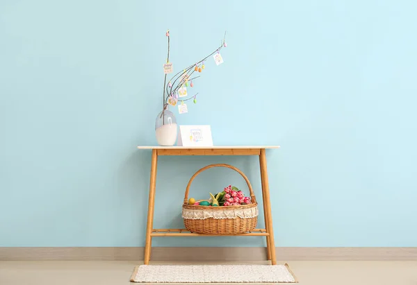 青い壁の近くのテーブルの上にイースターの卵と花の花瓶とウィッカーバスケット — ストック写真