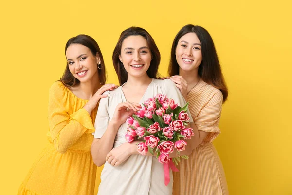 黄色の背景に花の花束を持つ美しい女性 国際女性デーのお祝い — ストック写真