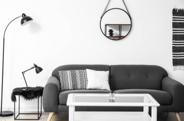 Beyaz duvarın yanındaki gri koltuklu şık bir iç mekan.