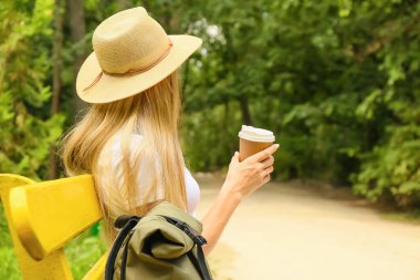 Kahveli kadın turist parkta bankta oturuyor.