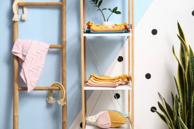 Renkli duvarın yanında şirin bebek kıyafetleri olan raf ünitesi.