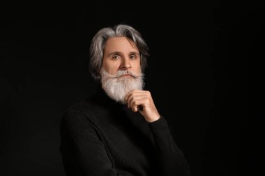 Siyah arka planda yakışıklı, olgun, sakallı bir adamın portresi.