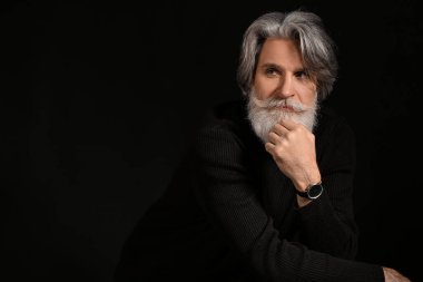 Siyah arka planda yakışıklı, olgun, sakallı bir adamın portresi.