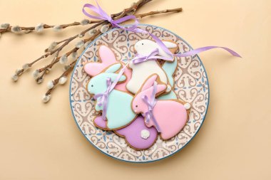Plate with tasty Easter cookies in shape on bunny and pussy willow branches on beige background