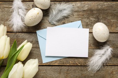 Güzel Paskalya kompozisyonu, boş bir kart, tahta arka planda yumurtalar ve çiçekler.