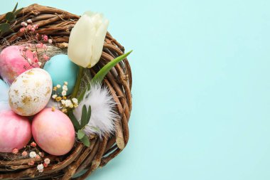 Mavi arka planda boyanmış Paskalya yumurtaları ve çiçekli yuva