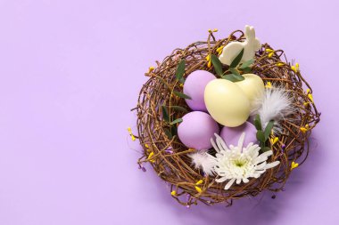 Mor arka planda boyanmış Paskalya yumurtaları, tavşan ve çiçekli yuva.
