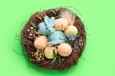 Yeşil arka planda boyanmış Paskalya yumurtaları, tavşan ve çiçeklerle dolu bir yuva.