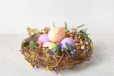 Işıklı arka planda boyanmış Paskalya yumurtaları ve çiçekleri olan yuva