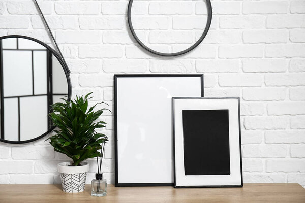Houseplant, picture frames, reed diffuser on desk and mirror on brick wall background