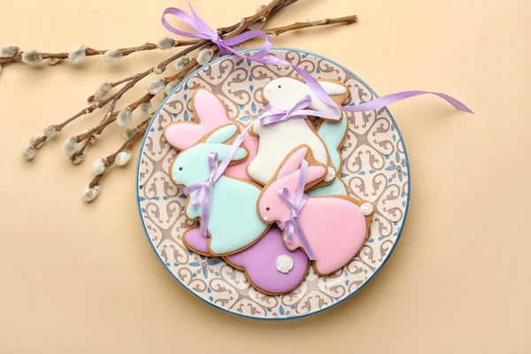 Plate with tasty Easter cookies in shape on bunny and pussy willow branches on beige background