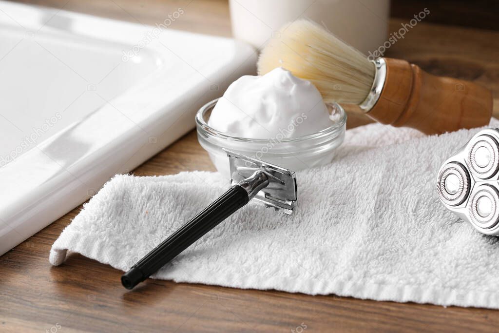 Shaving razor, towel and foam on table in bathroom