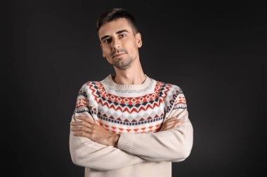 Esmer arka planda örülü süveter giyen yakışıklı bir genç.