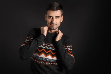 Esmer arka planda örülü süveter giyen yakışıklı bir genç.