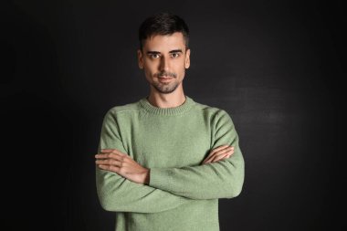 Esmer arka planda örülü süveter giyen yakışıklı bir genç.