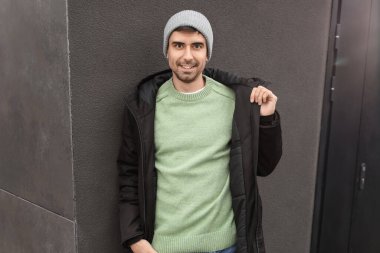 Esmer arka planda örülü süveter giyen yakışıklı bir genç.