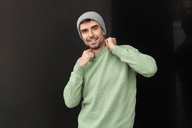 Esmer arka planda örülü süveter giyen yakışıklı bir genç.