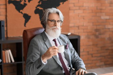 Yakışıklı, sakallı iş adamı ofiste kahve içiyor.