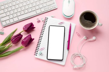 Cep telefonlu kompozisyon, bir fincan kahve, klavye ve pembe arka planda çiçekler