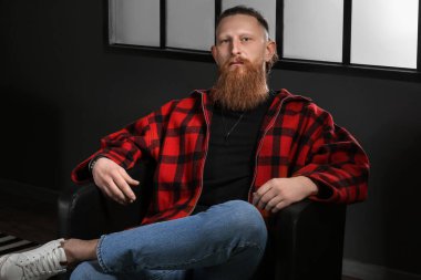 Evdeki koltukta oturan yakışıklı sakallı adamın portresi.