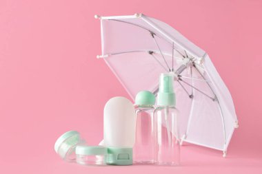 Pembe arka planda boş seyahat kozmetik şişeleri ve şemsiye seti