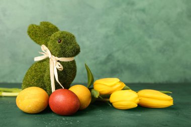 Güzel Paskalya tavşanı, lale çiçekleri ve yeşile boyanmış yumurtalar.