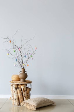 Ağaç dallı vazo, renkli Paskalya yumurtası ve sepeti ışık duvarının yanındaki masada.