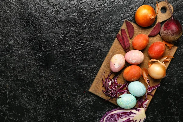 Tahta tahta tahta tahta, güzel Paskalya yumurtaları ve koyu arkaplanda doğal boyalar.
