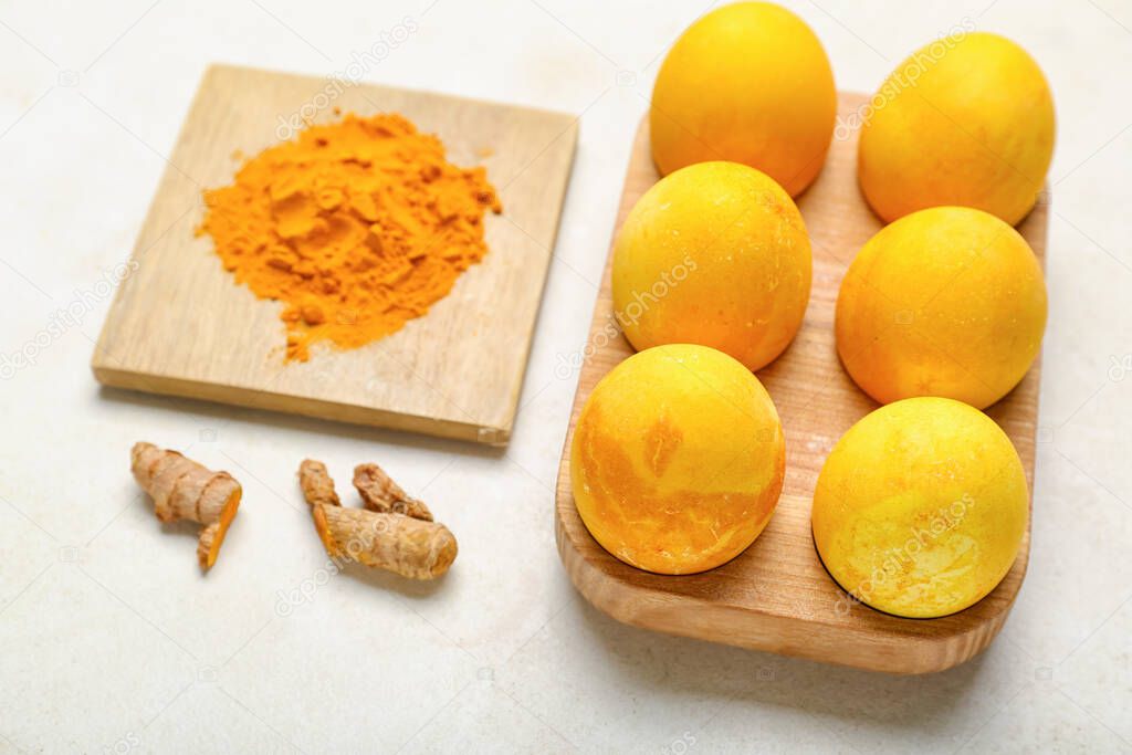 Wooden holder with beautiful Easter eggs and turmeric powder on light background, closeup
