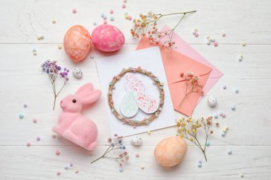 Güzel Paskalya kompozisyonu tebrik kartı, boyalı yumurta, tavşan ve çiçek açık ahşap arka planda