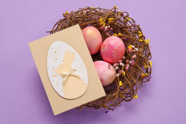 Boyanmış Paskalya yumurtaları ve mor arka planda tebrik kartı olan bir yuva.
