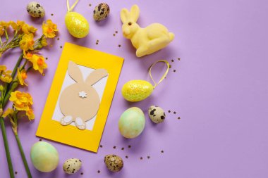 Güzel Paskalya kompozisyonu, tebrik kartı, boyalı yumurta, tavşan ve mor arka planda çiçekler.