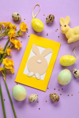 Güzel Paskalya kompozisyonu, tebrik kartı, boyalı yumurta, tavşan ve mor arka planda çiçekler.