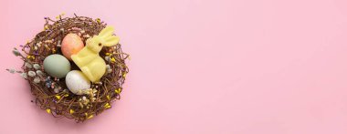 Renkli Paskalya yumurtaları ve pembe arka planda tavşanlı yuvada mesaj için yer var.